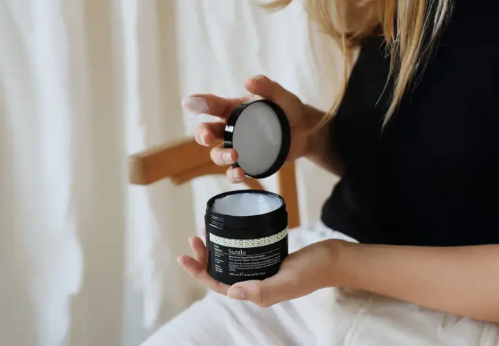 Kobieta z blond włosami kręconymi otwiera słoiczek z maską do włosów.