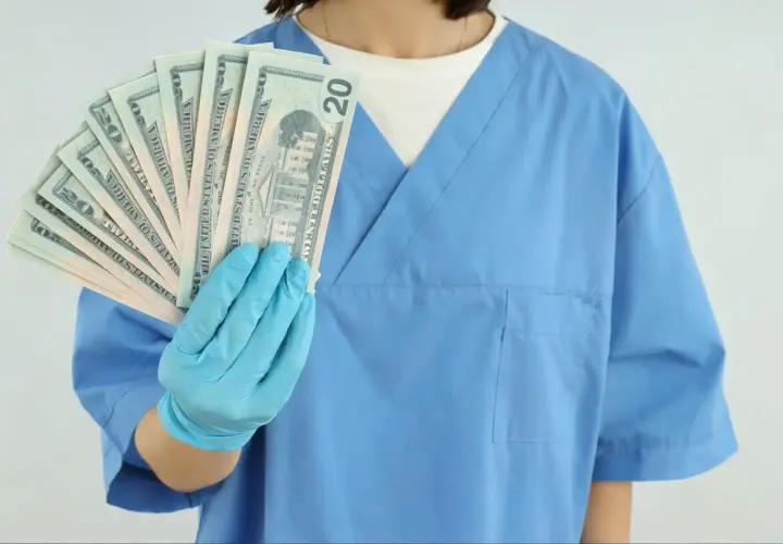 Higienistka stomatologiczna w niebieskim fartuchu pokazuje banknoty dwudziestodolarowe. Zastanawiasz się, ile zarabia higienistka stomatologiczna?