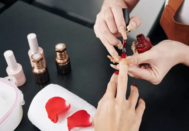 Manicure w trakcie. Stylistka nakłada czerwony lakier. Zastanawiasz się, jak przyspieszyć wysychanie lakieru do paznokci?