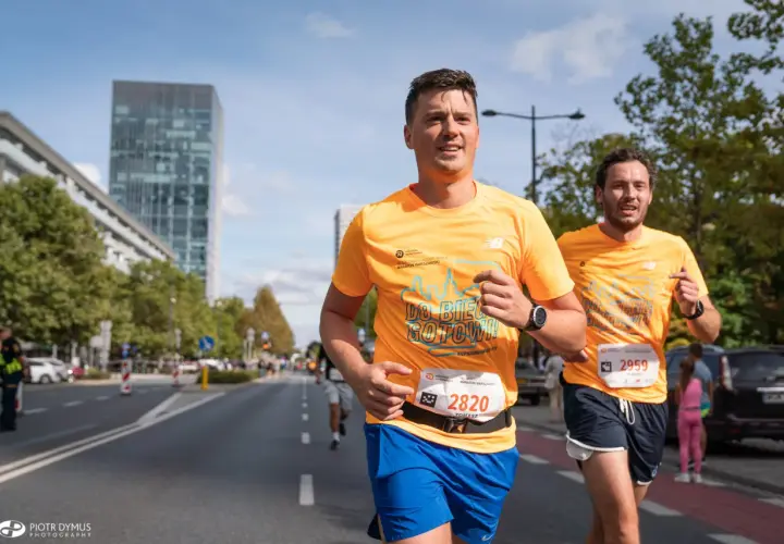 Dwóch biegaczy w pomarańczowych koszulkach na ulicach Warszawy podczas maratonu. Czy to już 42 maraton ile km?
