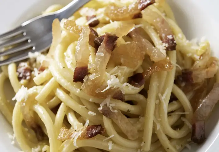 Ein Teller Pasta mit knusprigen Speckwürfeln, die zeigen, was ist Guanciale: luftgetrockneter Schweinebackenspeck, der für den authentischen Geschmack sorgt.