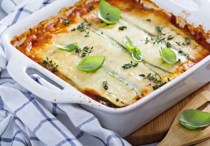 Pasticcio di zucchine appena sfornato, dorato e filante, guarnito con basilico fresco e timo.