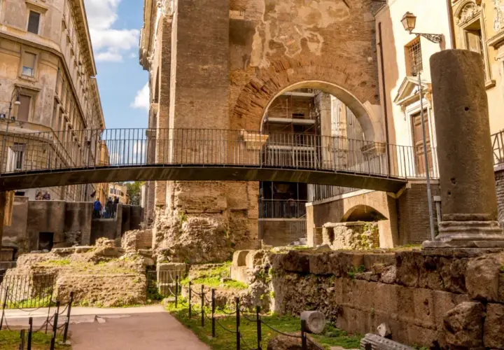 Antiche rovine nel ghetto ebraico di Roma, cosa vedere: un ponte moderno attraversa resti di colonne e mura di mattoni.