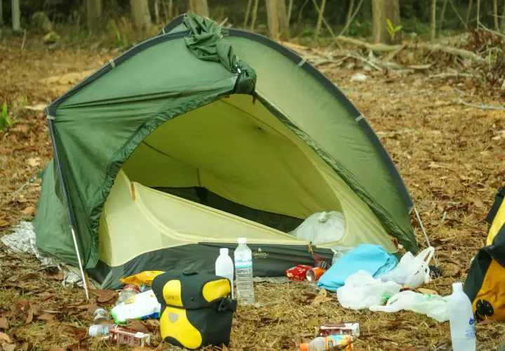Zielony namiot VAUDE rozbity na leśnej polanie, wokół śmieci. Jaki namiot, taki biwak.