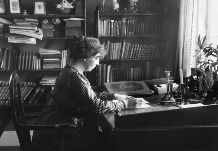 Norwegische Schriftstellerin Sigrid sitzt an ihrem Schreibtisch, umgeben von Büchern, und schreibt.