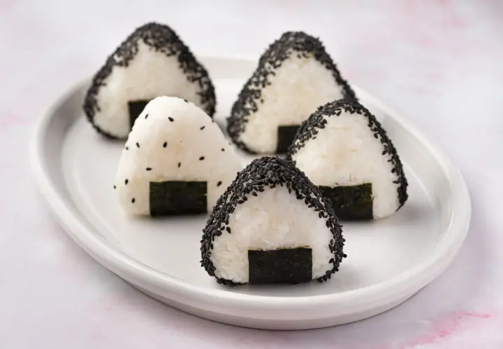 Five triangular rice balls, some coated in black sesame seeds, sit on a white plate. This is what a rice ball looks like.