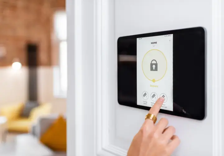 Main d'une personne touchant un écran tactile pour activer un système d'alarme filaire ou sans fil.
