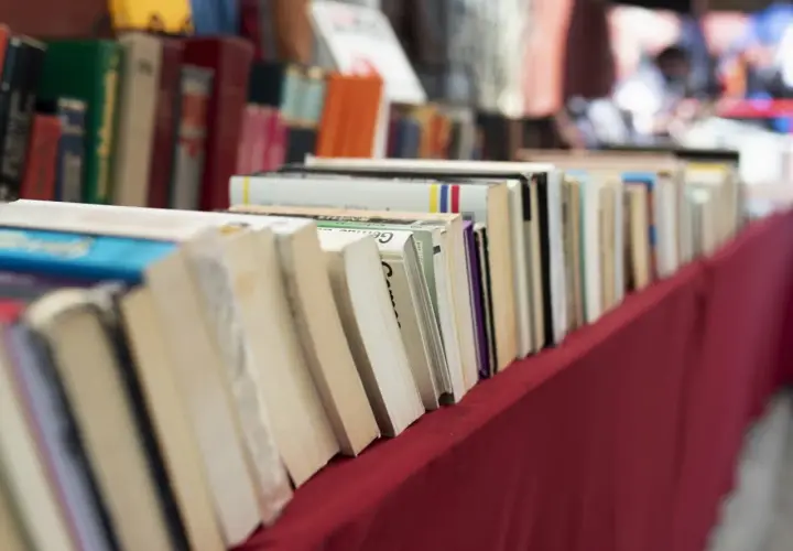 Rząd książek na czerwonym obrusie. Jak przygotować się do targów książki jako autor i czytelnik?