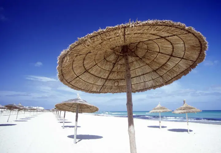 Słomiane parasole na białej plaży, błękitne niebo i morze. Idealna pogoda Tunezja marzec na relaks.