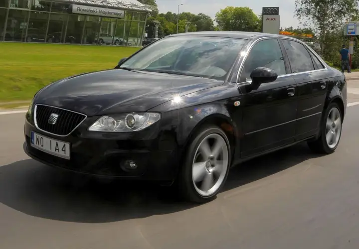Czarny Seat Exeo 2.0 TDI w ruchu, z widocznym salonem Audi w tle.