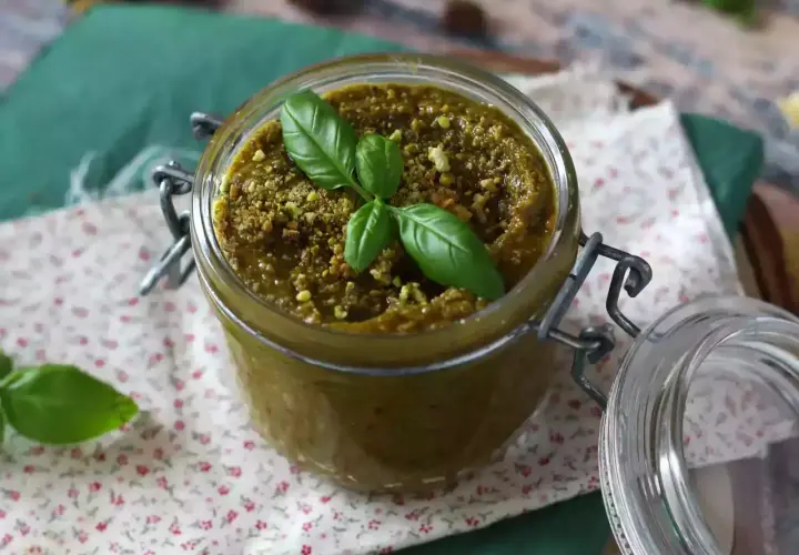 Słoik z pysznym, domowym pesto pistacjowym, ozdobiony listkami bazylii. Idealne do makaronu i kanapek.