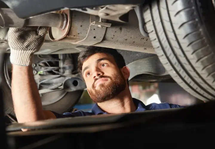 Mechanik w rękawiczce sprawdza podwozie samochodu, wykonując naprawę układu wydechowego.