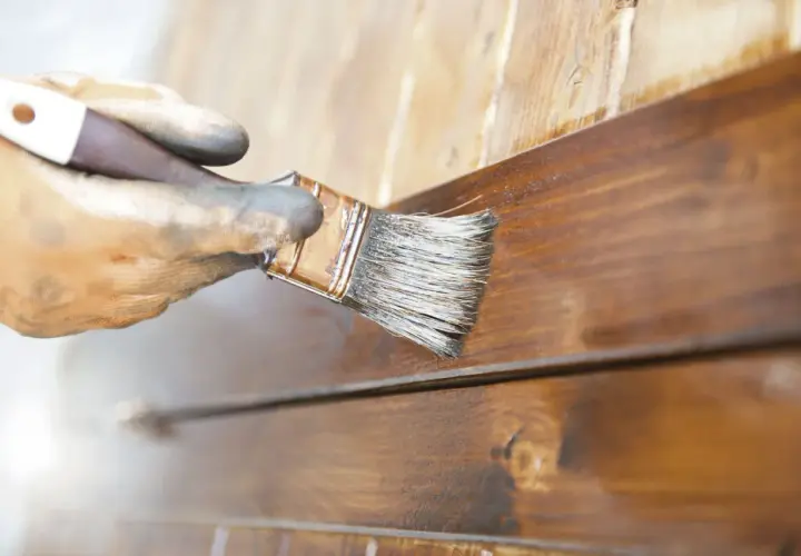 Mano enguantada aplica barniz a madera. El proceso de lijar entre capas de barniz asegura un acabado perfecto.