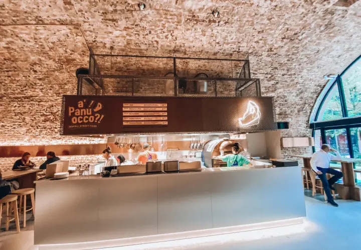 Wnętrze jednej z nowych restauracji w Warszawie. Widać piec do pizzy, bar i gości.