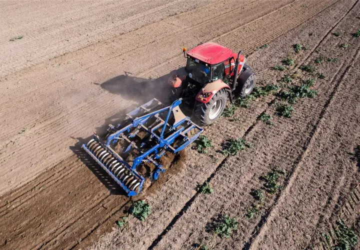 Un tracteur rouge travaille le sol avec un cultivateur, préparant le terrain pour la culture sans labour.