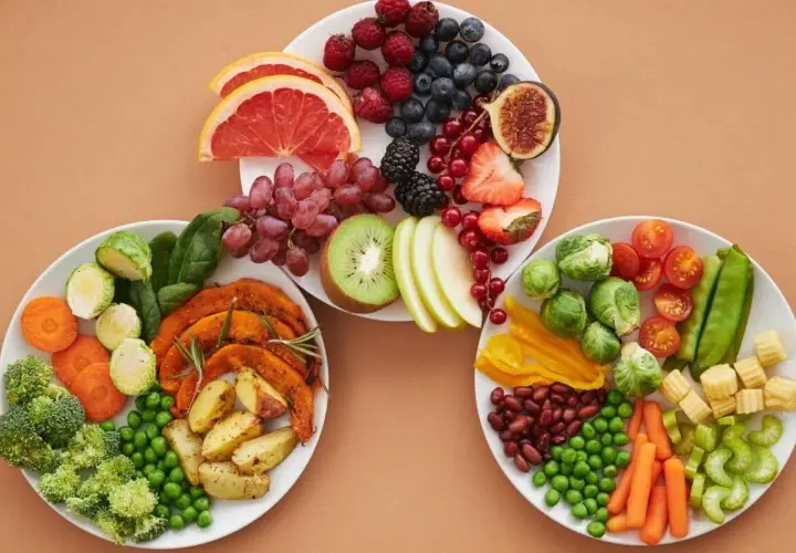 Platos con frutas y verduras frescas, incluyendo arándanos, fresas, uvas, kiwi, brócoli, zanahorias y guisantes. Una selección de alimentos diuréticos para una dieta saludable.