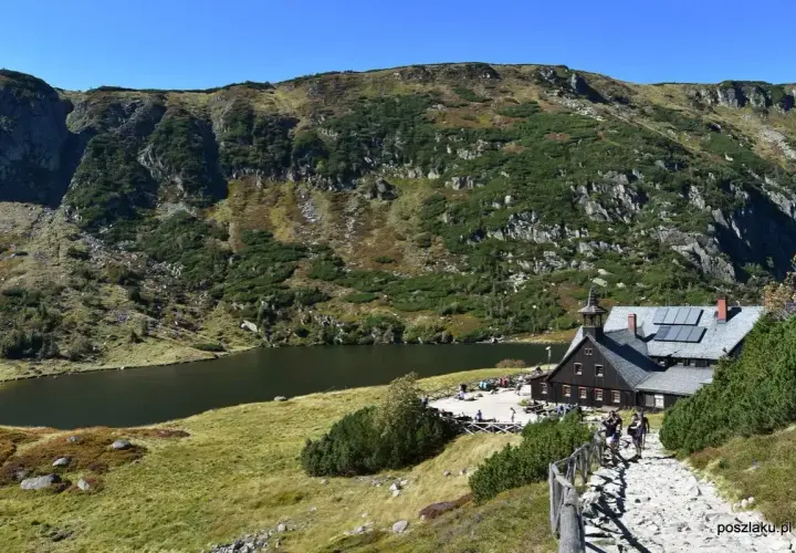 Schronisko Samotnia nad Małym Stawem w Karkonoszach. Kamienista ścieżka prowadzi do schroniska, obok którego rozciąga się malownicze jezioro.