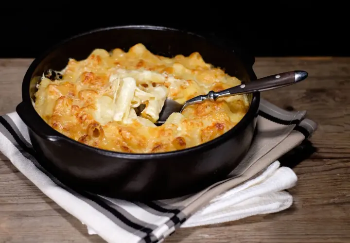 Un plat réconfortant de gratin de pâtes à l'ancienne, doré et gratiné au fromage, servi dans un plat noir avec une cuillère.