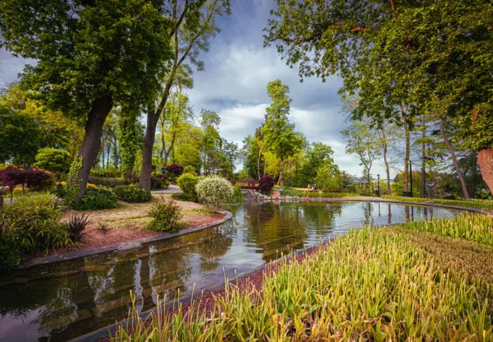 Malowniczy park z jeziorem, mostkiem i bujną zielenią.
