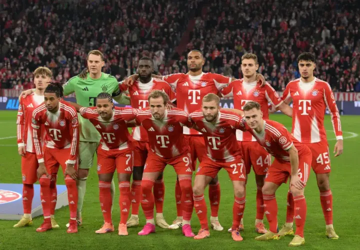 Drużyna Bayern Monachium – zawodnicy w czerwono-białych strojach pozują do zdjęcia na murawie stadionu, z trybunami pełnymi kibiców w tle.