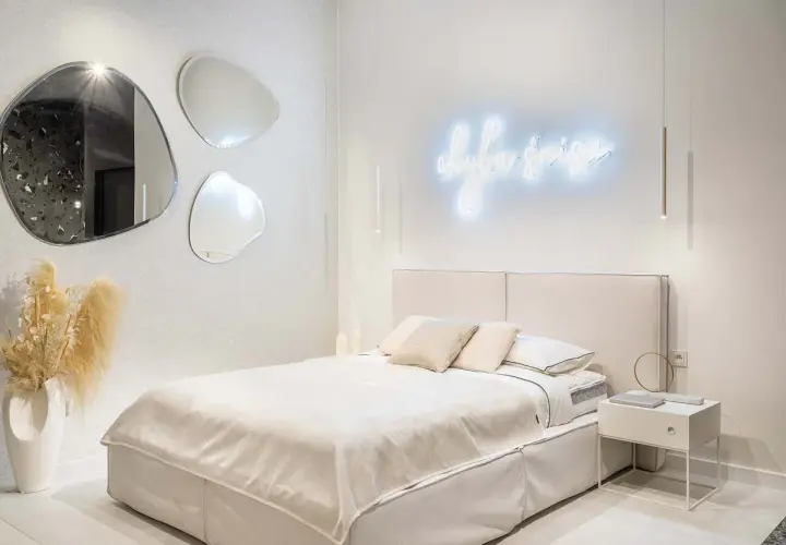 Nowoczesne oświetlenie sypialni inspiracje: neonowy napis, wiszące lampy i lustra o organicznych kształtach tworzą przytulną atmosferę.
