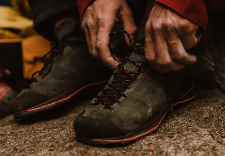 Hands tying red-laced hiking boots. Proper fit is crucial for comfort and performance on the trail.