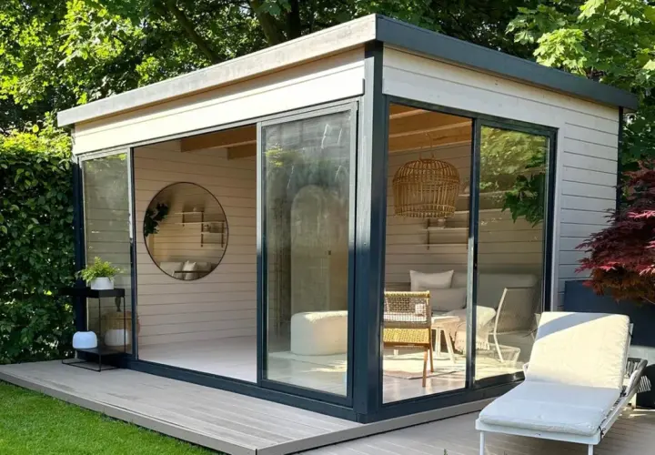 Modernes Gartenhaus mit Glasfront, das zum Streichen einlädt. Gemütliche Inneneinrichtung mit Rattan-Akzenten und Liegestuhl im Freien.