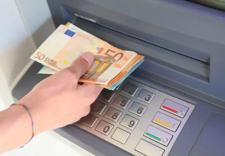 Dłoń trzyma banknoty 50 euro, walutę Hiszpanii, przy bankomacie.
