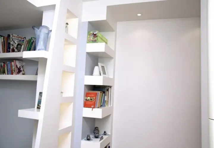 Scaffali moderni in cartongesso, con libri, vasi e soprammobili, creano un angolo lettura accogliente.