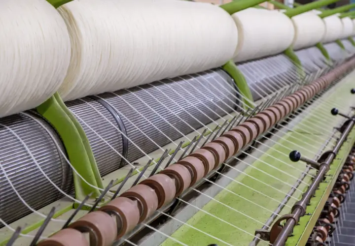 Gros rouleaux de fil blanc sur une machine de filature. Le processus de filature est en cours, transformant la matière première en fil.