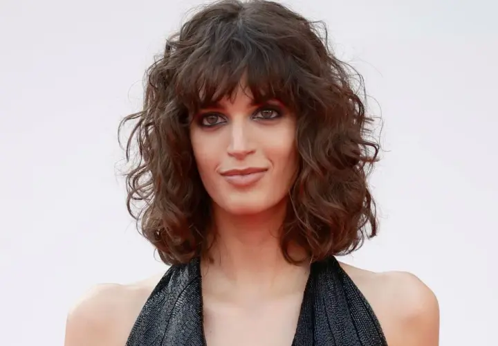Mujer con curly pelo corto rizado natural, mirada intensa y vestido negro brillante.