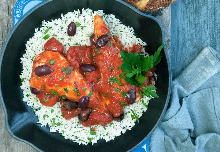 Un plat de poulet sauce tomate savoureux, servi sur un lit de riz blanc, garni d'olives noires et de persil frais.