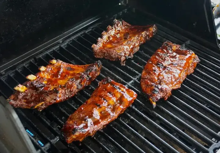 Soczyste żeberka w marynacie do żeberek skwierczą na grillu, nabierając apetycznego koloru.