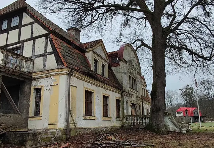 Zniszczony dworek w Paraszyne, z charakterystyczną architekturą i opadającą fasadą, otoczony drzewami.