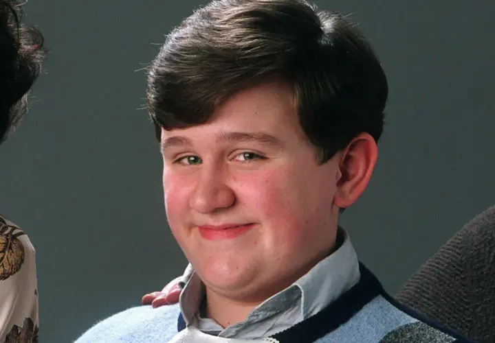 Uśmiechnięty Dudley Dursley, kuzyn Harry'ego Pottera, w niebieskim swetrze.