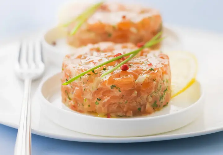Deux tartares de saumon frais, garnis de ciboulette et de poivre rose, prêts à être dégustés. Parfait pour savoir que boire avec un tartare de saumon.