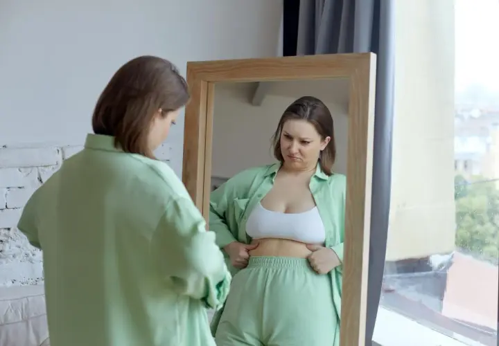 Kobieta w lustrze analizuje swoje ciało, szukając oznak spalania tłuszczu.