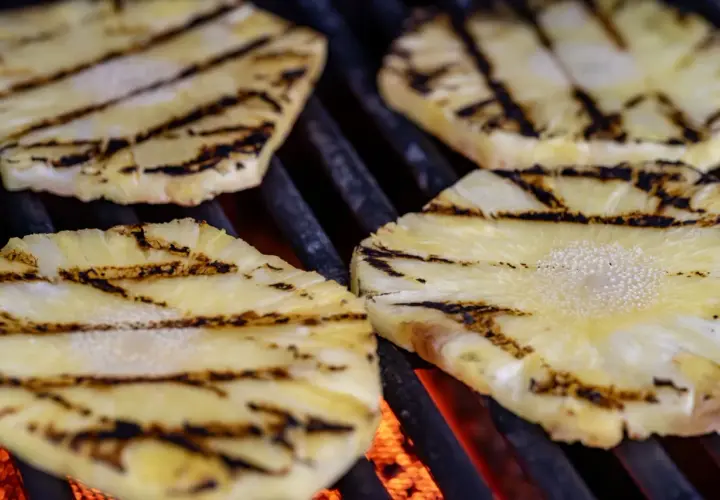 Tranches d'ananas barbecue grillées, avec des marques de cuisson foncées sur fond de braises rougeoyantes.