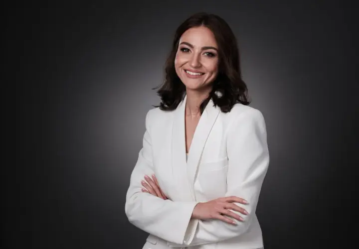 Uśmiechnięta kobieta w białej marynarce, z rękami skrzyżowanymi na piersi. Idealny przykład, jak pozować do zdjęć, by wyglądać profesjonalnie i pewnie.