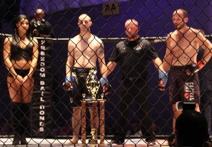 Ring girls i zawodnicy MMA czekają na rozpoczęcie freak fight. Trofeum lśni w blasku reflektorów.