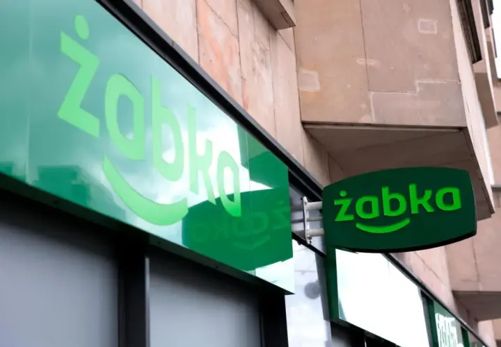 Zielony neon z logo Żabki. Zastanawiasz się, od ilu lat można pracować w Żabce? Odpowiedź znajdziesz w tym sklepie.