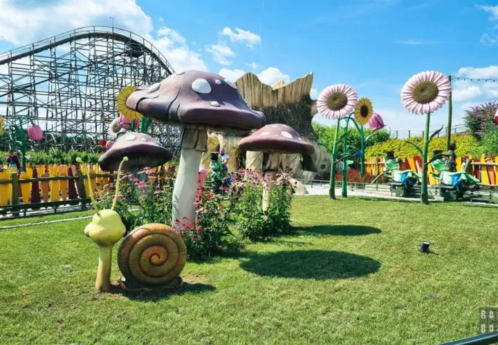 Park rozrywki z kolejką górską, wielkimi grzybami i bajkowymi dekoracjami.