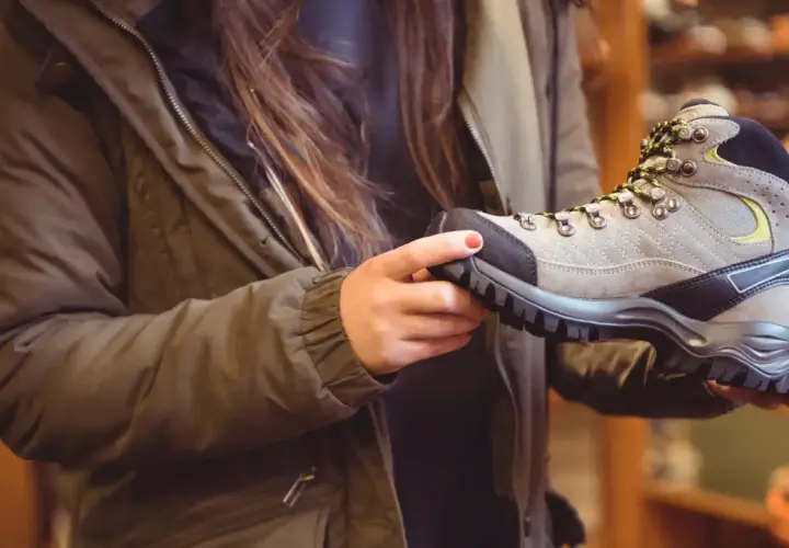 A person in a green jacket holds a hiking boot, considering if boots should fit snug or loose for comfort on the trail.