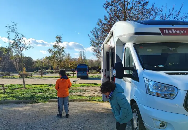 Deux enfants devant un camping-car Challenger, en route pour une aventure dans le sud de la France. Le soleil brille, les arbres perdent leurs feuilles.