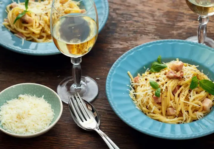 Un délicieux vin blanc accompagne un plat de spaghetti carbonara, garni de parmesan râpé et de basilic frais.