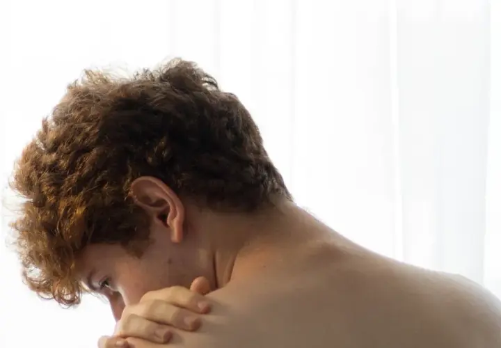 Close-up of a young person's back and neck, with a hand touching their shoulder.