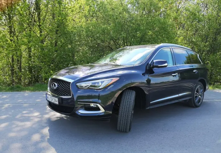 Ciemny Infiniti QX60 zaparkowany na poboczu drogi, otoczony zielenią drzew.