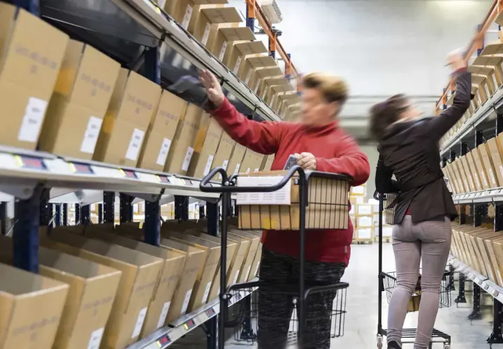 Mitarbeiter im Lager führen pick & pack aus, greifen Kartons aus Regalen und legen sie in Wagen.