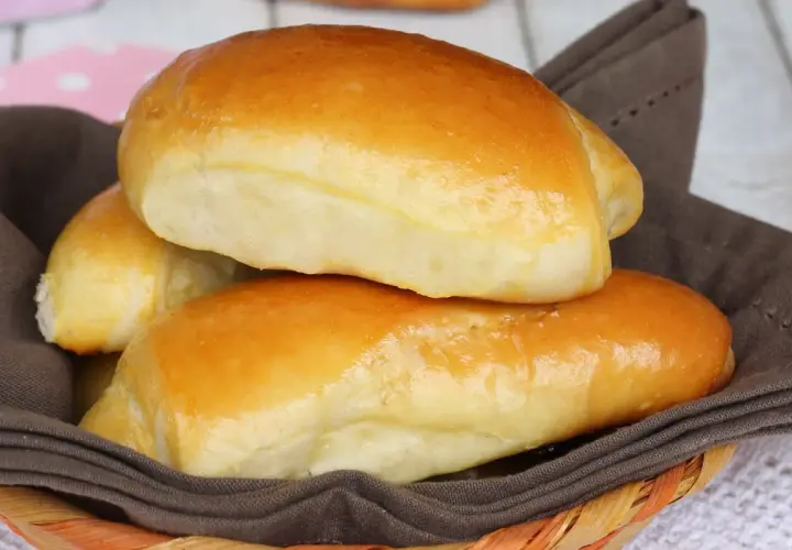 Deliziosi panini al latte dorati, morbidi e invitanti, serviti in un cestino foderato con un tovagliolo marrone.