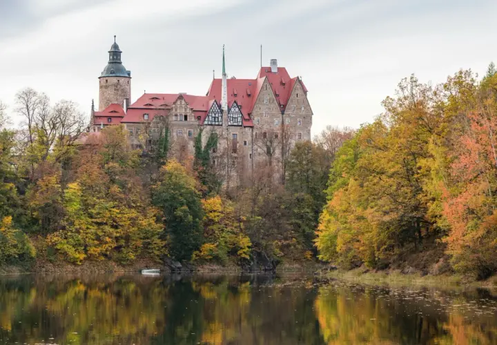Zamek Kliczków w jesiennej odsłonie, idealne miejsce na jednodniowy wypad w Polsce. Otoczony kolorowymi drzewami, odbija się w spokojnej tafli wody.